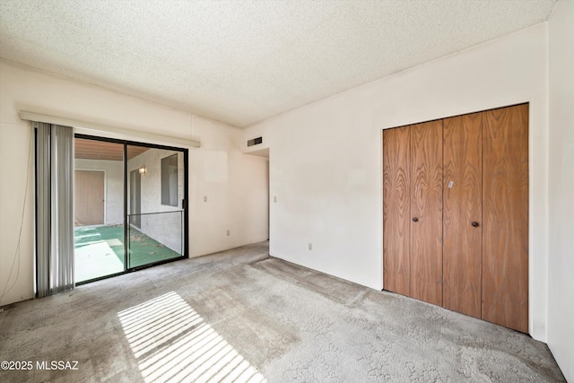 unfurnished bedroom with a textured ceiling, access to outside, carpet flooring, and visible vents