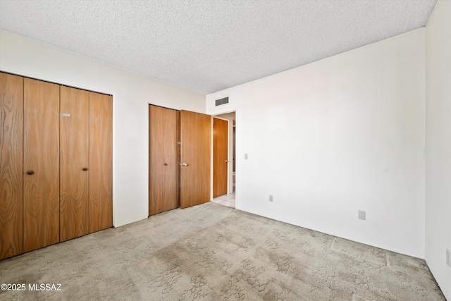 unfurnished bedroom featuring a textured ceiling, carpet, visible vents, and multiple closets