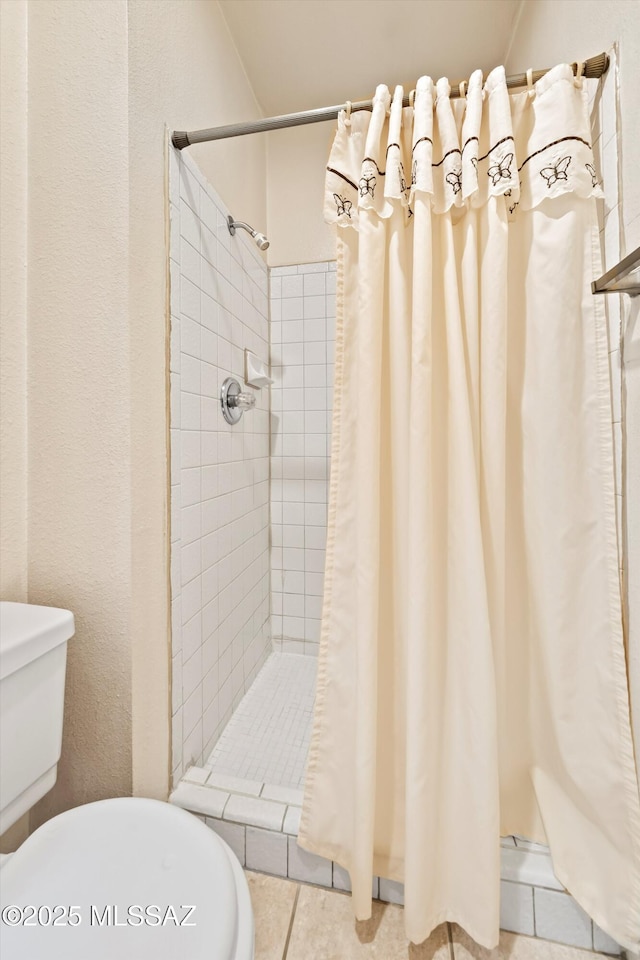 bathroom with a stall shower, tile patterned flooring, a textured wall, and toilet