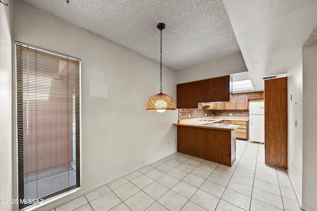 kitchen featuring light tile patterned flooring, a peninsula, hanging light fixtures, backsplash, and freestanding refrigerator