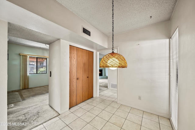 unfurnished dining area with light tile patterned floors, a textured ceiling, visible vents, and light colored carpet