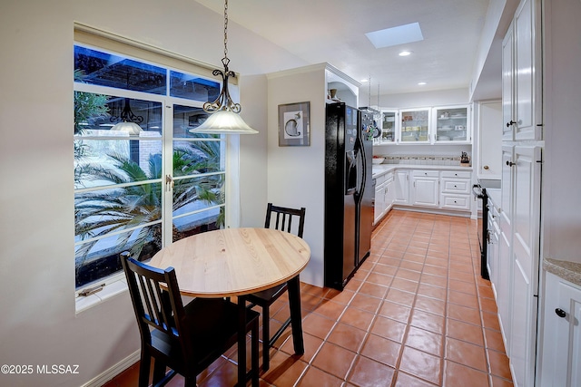 kitchen featuring a skylight, decorative light fixtures, light tile patterned floors, black fridge with ice dispenser, and white cabinetry