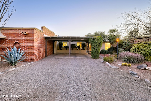 back of house with gravel driveway and brick siding