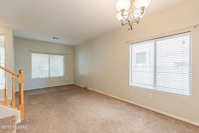 spare room featuring carpet floors, a wealth of natural light, stairway, and an inviting chandelier