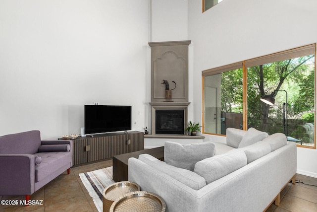 living room featuring a towering ceiling, tile patterned floors, and a glass covered fireplace