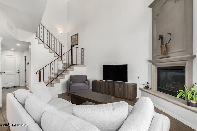 living area with baseboards, a glass covered fireplace, stairway, a high ceiling, and recessed lighting