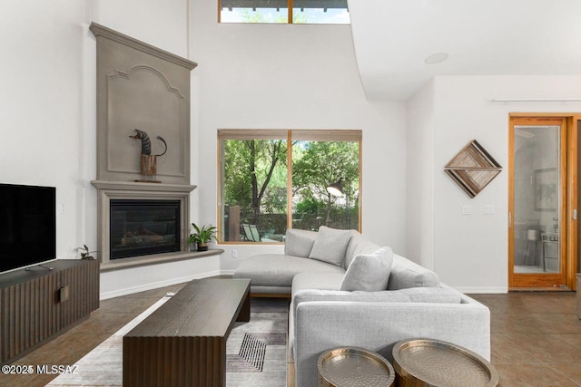 tiled living area featuring a high ceiling, baseboards, and a glass covered fireplace