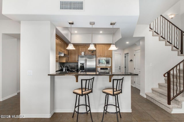 kitchen featuring visible vents, brown cabinetry, appliances with stainless steel finishes, a peninsula, and a kitchen bar