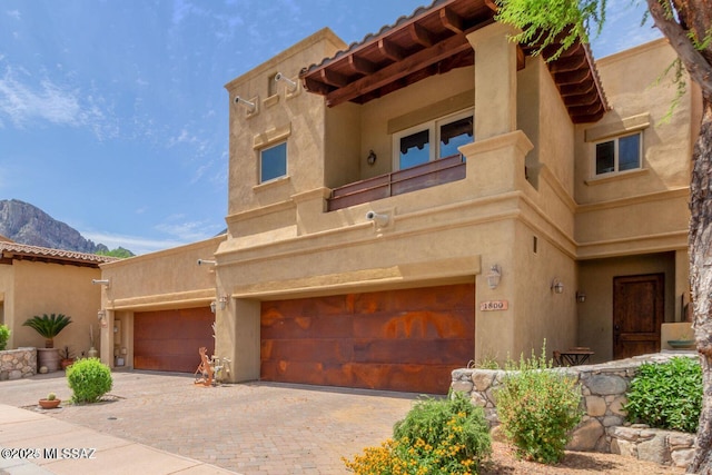 pueblo-style house featuring an attached garage, decorative driveway, and stucco siding