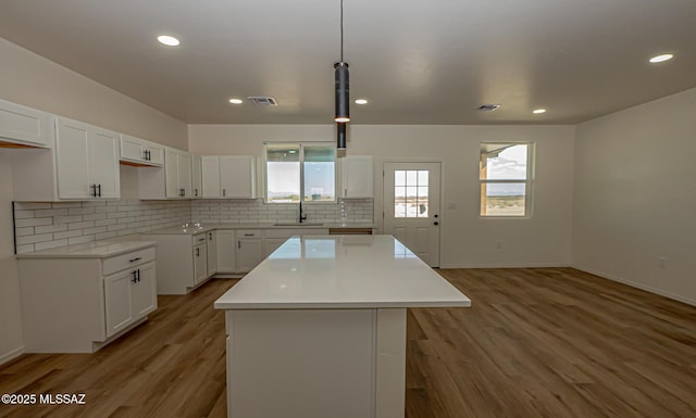 kitchen with a sink, light wood-style floors, a kitchen island, and tasteful backsplash