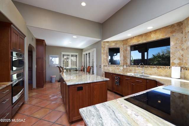 kitchen with arched walkways, black electric stovetop, light stone counters, a sink, and decorative backsplash