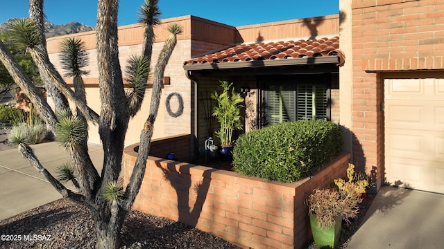 entrance to property featuring brick siding, a tiled roof, and an attached garage