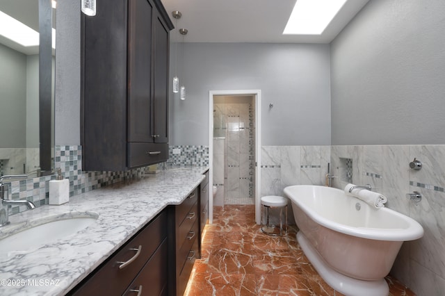 full bathroom featuring a skylight, vanity, a freestanding tub, a shower stall, and tile walls