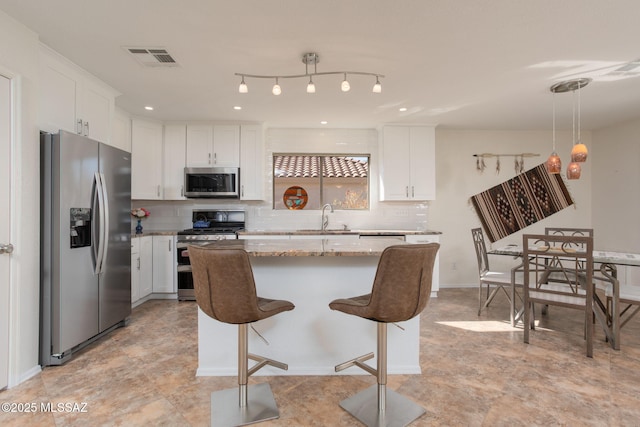 kitchen featuring light stone counters, a sink, white cabinetry, appliances with stainless steel finishes, and decorative light fixtures