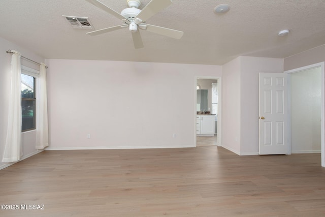 spare room with a textured ceiling, ceiling fan, visible vents, baseboards, and light wood-type flooring