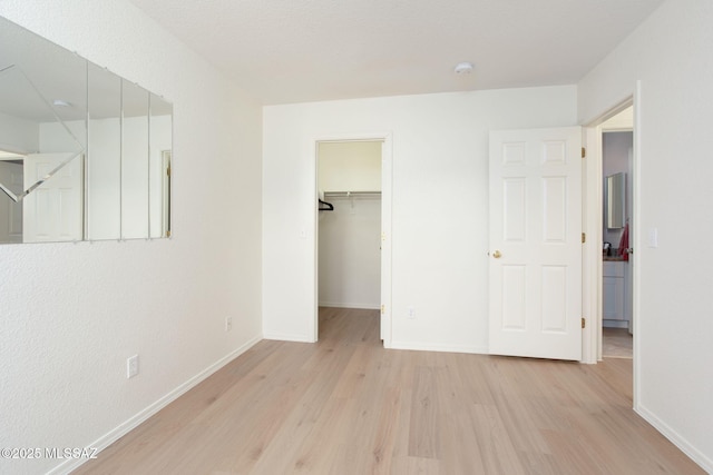 unfurnished bedroom with light wood-type flooring, baseboards, a walk in closet, and a closet