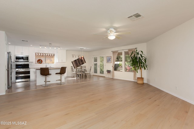 unfurnished living room with visible vents, a sink, light wood finished floors, and ceiling fan