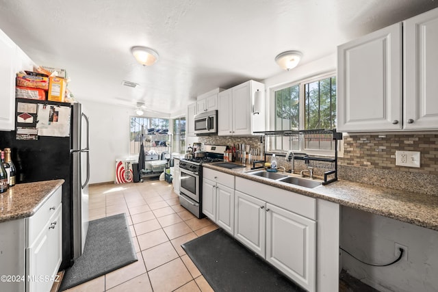 kitchen with backsplash, appliances with stainless steel finishes, white cabinetry, a sink, and light tile patterned flooring