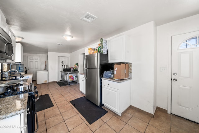 kitchen with appliances with stainless steel finishes, white cabinets, visible vents, and light tile patterned flooring