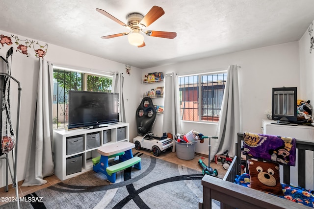 playroom featuring ceiling fan, a textured ceiling, tile patterned flooring, and a healthy amount of sunlight