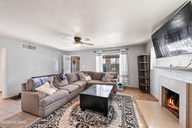 living area featuring a textured ceiling, a high end fireplace, visible vents, and a ceiling fan