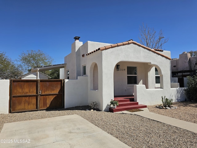 view of front of property featuring a tile roof, a gate, fence, and stucco siding