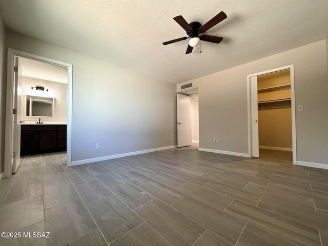 unfurnished bedroom featuring ensuite bathroom, a sink, visible vents, baseboards, and a walk in closet