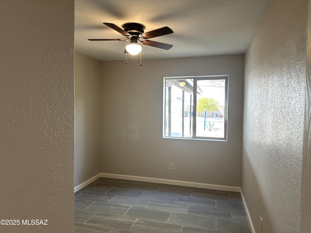 empty room featuring a textured wall, baseboards, and ceiling fan