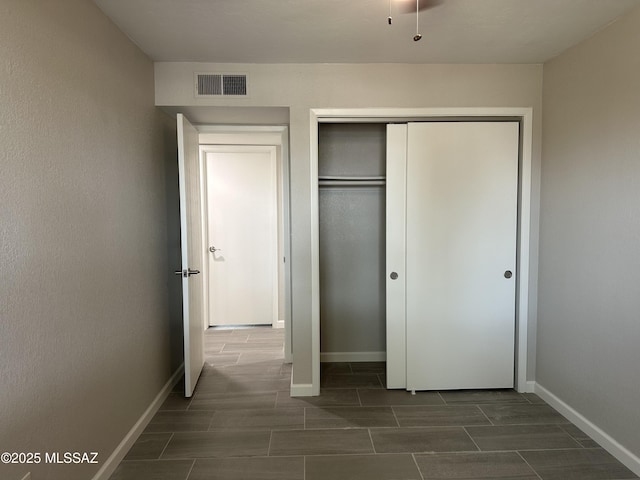 unfurnished bedroom featuring wood finish floors, a closet, visible vents, and baseboards