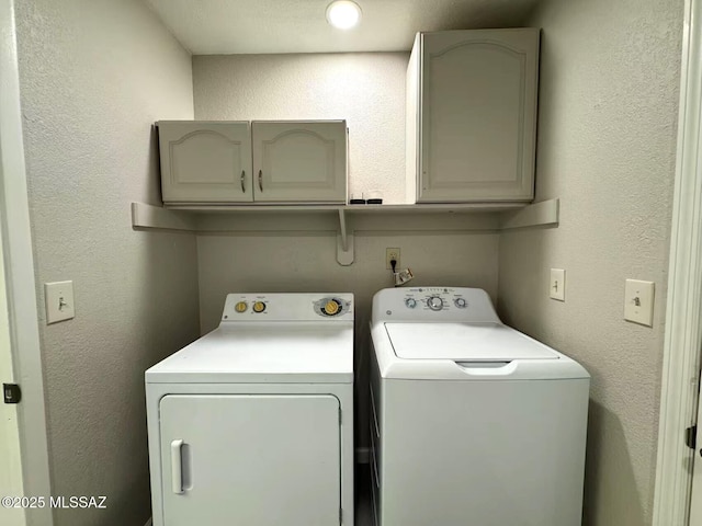 laundry area with a textured wall, cabinet space, and washer and dryer