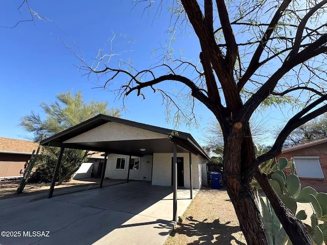 view of front of home featuring driveway, an attached carport, fence, and stucco siding