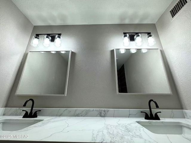 bathroom featuring vanity, visible vents, a textured ceiling, and a textured wall