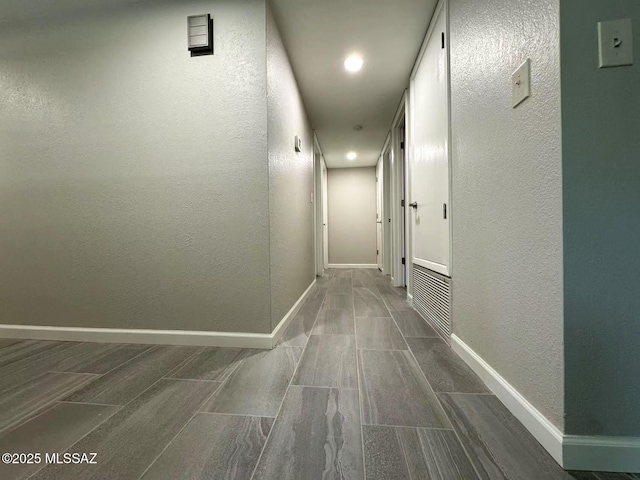 hall with wood tiled floor, baseboards, and a textured wall