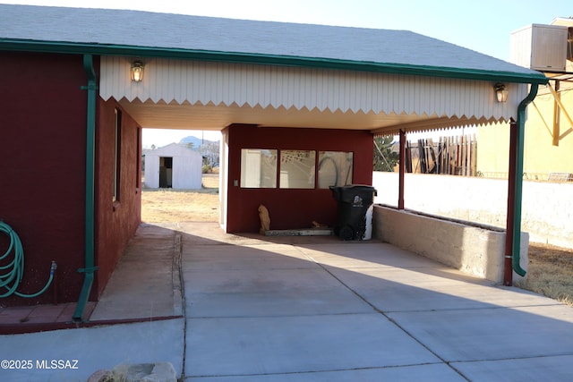 view of patio with an attached carport, cooling unit, an outdoor structure, concrete driveway, and a shed