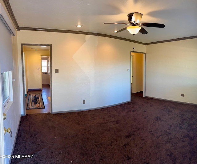 unfurnished room with ornamental molding, dark carpet, baseboards, and ceiling fan