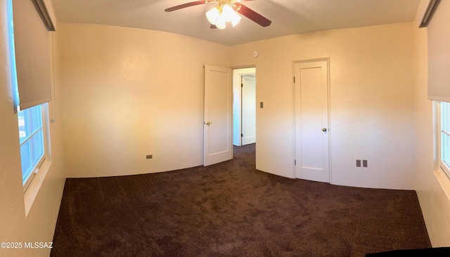 unfurnished bedroom with a closet, dark carpet, and ceiling fan