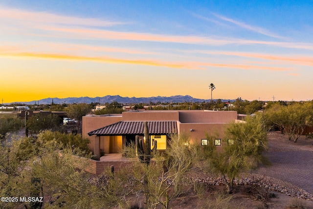 pueblo-style home with a tiled roof, a mountain view, and stucco siding