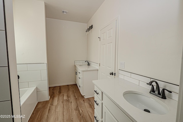 bathroom with two vanities, wood finished floors, a sink, and visible vents