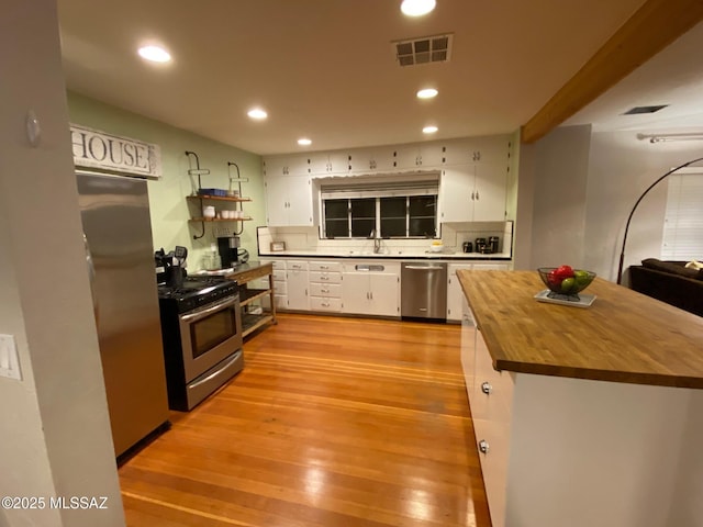 kitchen featuring light wood-style flooring, stainless steel appliances, wood counters, visible vents, and white cabinetry