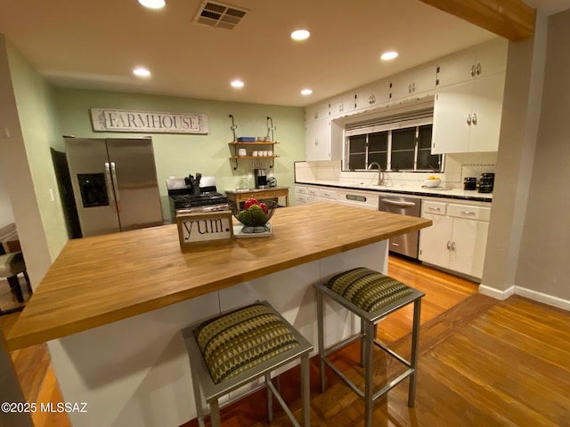 kitchen with wooden counters, appliances with stainless steel finishes, visible vents, and white cabinets