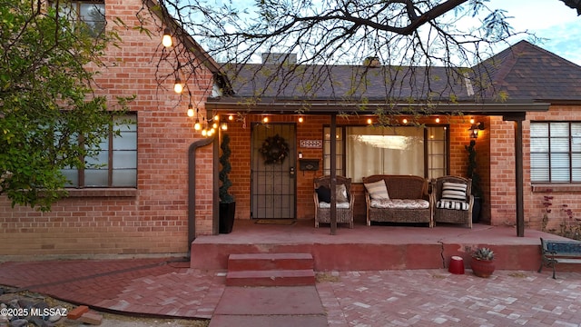 property entrance with a shingled roof, a porch, and brick siding