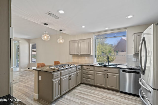 kitchen featuring visible vents, a peninsula, gray cabinets, a sink, and appliances with stainless steel finishes