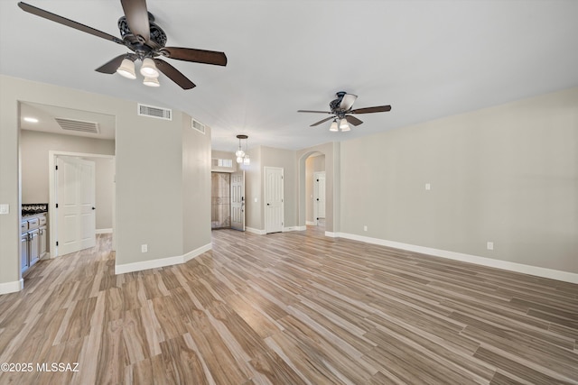 unfurnished living room featuring arched walkways, light wood finished floors, visible vents, and baseboards