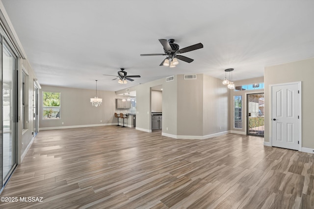 unfurnished living room with ceiling fan with notable chandelier, light wood-type flooring, visible vents, and a healthy amount of sunlight