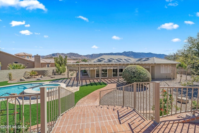 view of front facade with a fenced backyard, a patio area, a pool with connected hot tub, a mountain view, and stucco siding