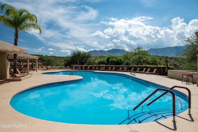 community pool with fence, a mountain view, and a patio