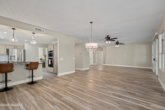 living area with light wood-style floors, visible vents, baseboards, and ceiling fan with notable chandelier