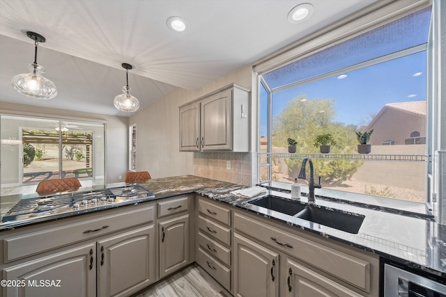 kitchen with pendant lighting, backsplash, gray cabinetry, a sink, and dark stone counters