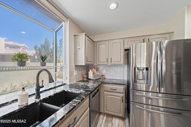 kitchen with decorative backsplash, stainless steel appliances, a sink, and dark stone counters