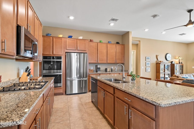 kitchen with stainless steel appliances, visible vents, brown cabinetry, a sink, and light stone countertops